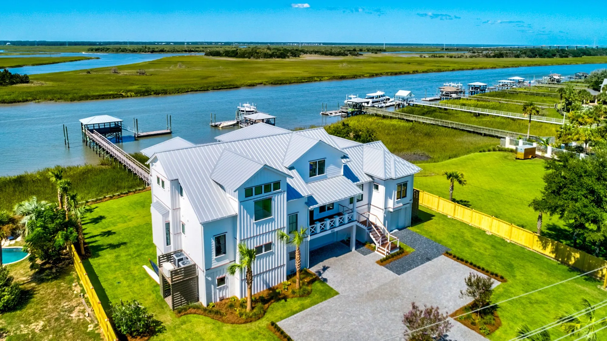 Drone view of a white coastal home with a long dock over the marsh to the waterway