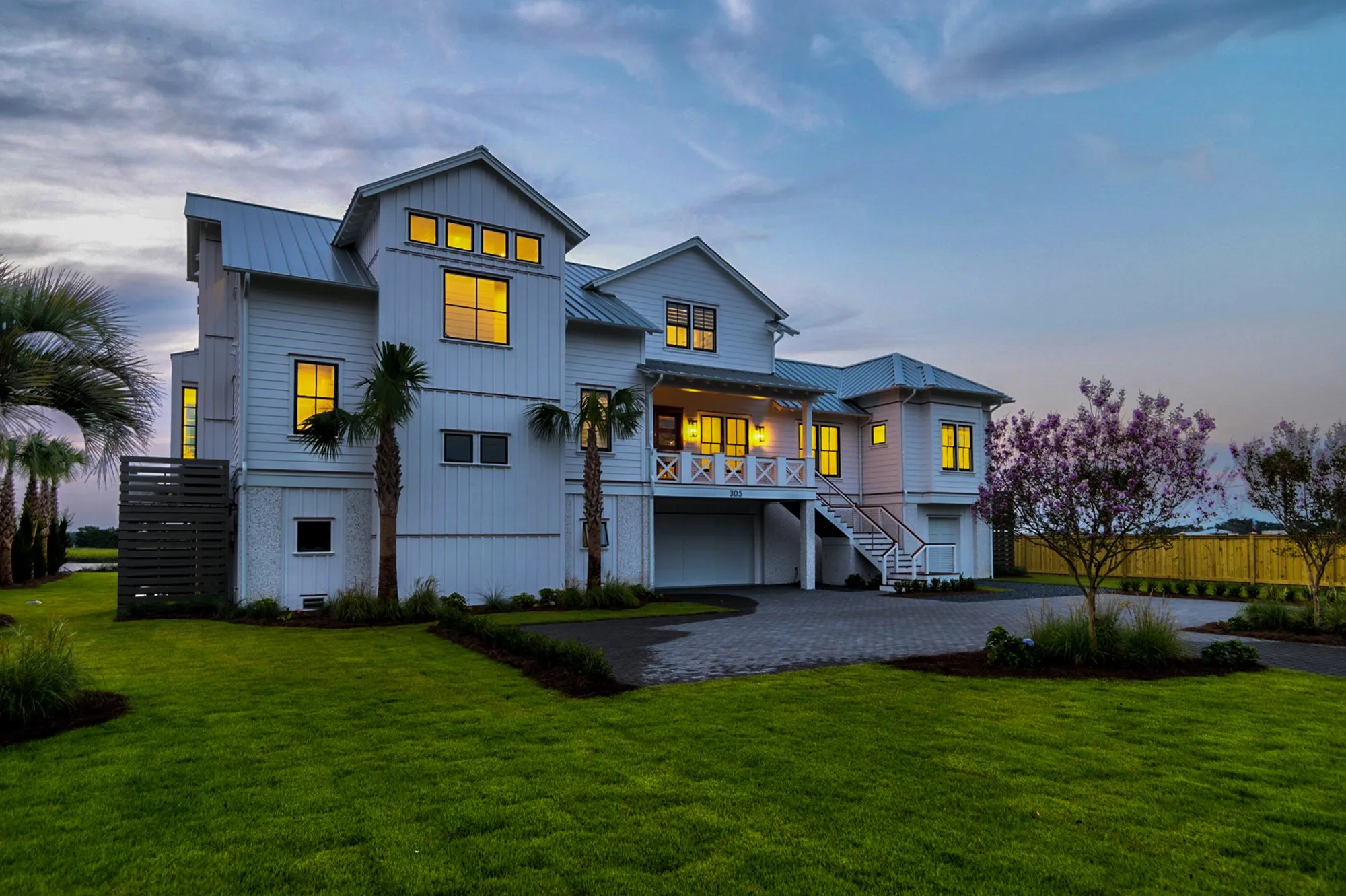 Front of a white board-and-batten home at dusk with every window lit