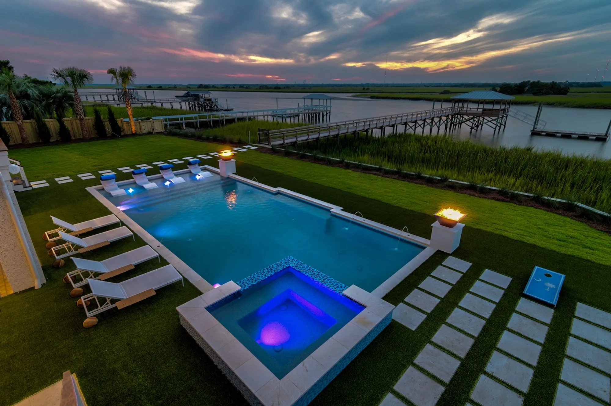Elevated twilight view of a pool and spa lit blue, with the marsh and docks beyond